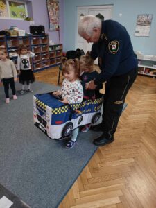 Dzieci zakładają strój (zabawkę) pojazdu straży miejskiej.