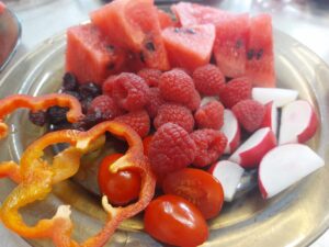 owocowo-warzywne talerze: pomidorki koktajlowe, rzodkiewka krojona na cząstki, arbuz, borówki oraz czerwona papryka krojona.