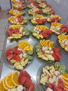 owocowo-warzywne talerze: plastry pomarańczy, arbuz krojony na cząstki, banan krojony na cząstki, połówki kiwi, pestki granata.