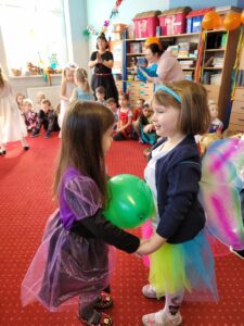 Para dziewczynek w kostiumach karnawałowych tańczy w parze z balonem między sobą.