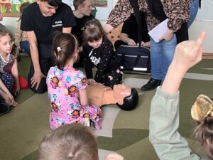 Dzieci pod nadzorem nauczycielki oraz uczniów Zespołu Szkół przy Teatralnej, ćwiczące RKO z wykorzystaniem fantoma.