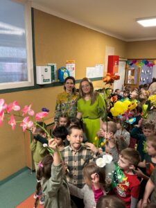 Dzieci trzymając w rękach kwiaty, podążają korytarzem przedszkola.