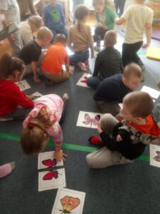 Dzieci siedząc na dywanie, układają z części w całość papierowe motyle.