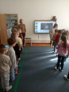Dzieci stojąc w dwóch rzędach, uczestniczą w zabawie ruchowej.