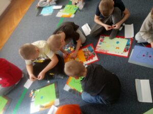 Dzieci siedząc na dywanie, wykonują pracę plastyczną - kolorowego motyla.